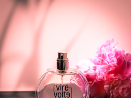 site-industries-cosmetiques Un frasco de perfume firmado en 4 diseños por Coverpla, Parfums Virevolte, colocado sobre una mesa junto a una flor rosa.