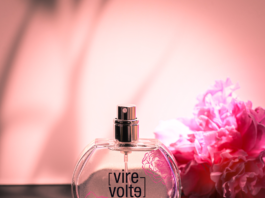 site-industries-cosmetiques A perfume bottle signed in 4 designs by Coverpla, Parfums Virevolte, sits on a table next to a pink flower.