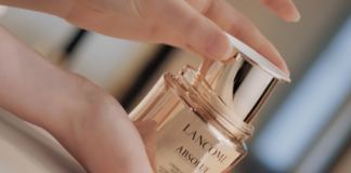 site-industries-cosmetiques La main d'une femme tenant une bouteille de cosmétiques en or.
