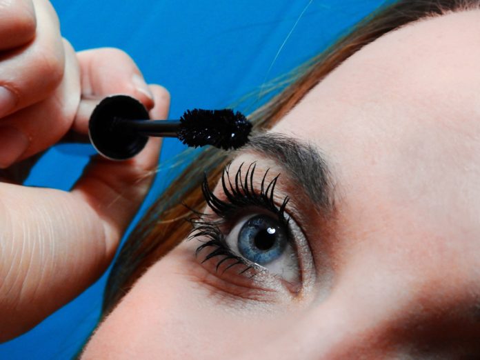 site-industries-cosmetiques A woman puts mascara on her eyes.