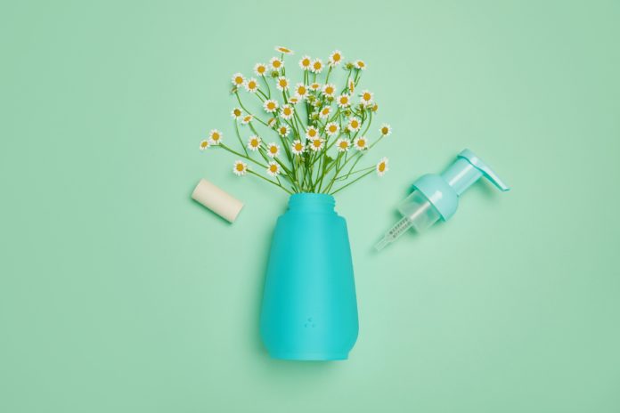 site-industries-cosmetiques Un vase bleu avec des fleurs et une bouteille de savon sur fond vert, avec Cosmogen comme partenaire.