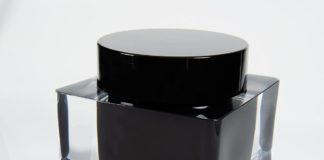 site-industries-cosmetiques Fabrico de um frasco de tinta preta com uma tampa transparente sobre uma superfície branca.