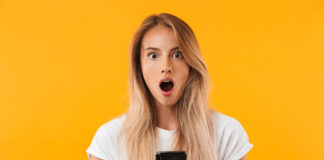 site-industries-cosmetiques A shocked woman checks her phone in front of an orange background.