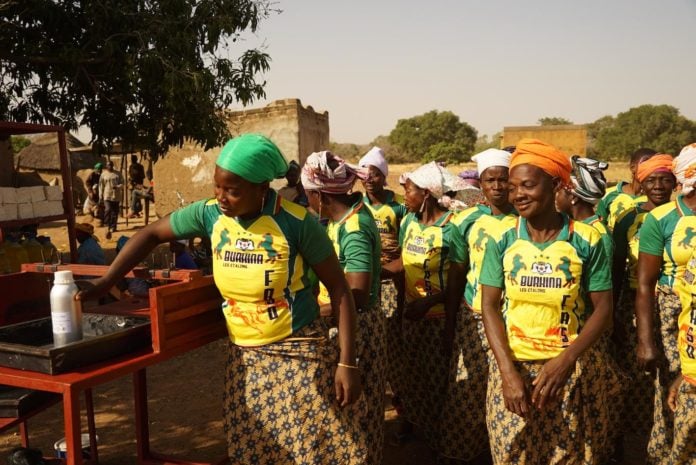 site-industries-cosmetiques Un groupe de femmes TechnicoFlor dans leurs chemises vertes et jaunes debout à côté d'un chariot, démontrant leur engagement envers les femmes du Burkina Faso.