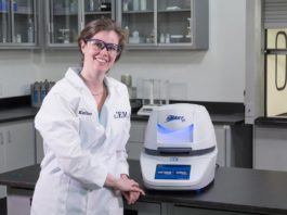 site-industries-cosmetiques Une femme en blouse de laboratoire utilisant une machine d'analyse pour mesurer la teneur en eau des échantillons.