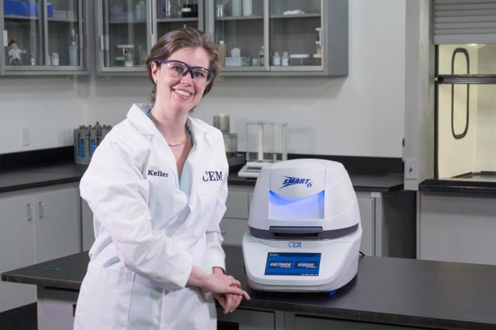 site-industries-cosmetiques Une femme en blouse de laboratoire utilisant une machine d'analyse pour mesurer la teneur en eau des échantillons.