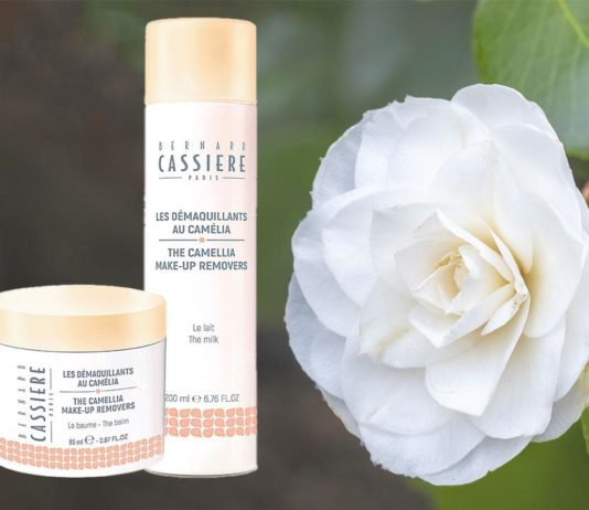 site-industries-cosmetiques Una flor blanca con un frasco de desmaquillante de aceite de camelia al lado.