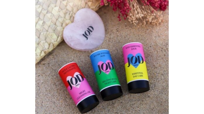 site-industries-cosmetiques Trois tubes de baume à lèvres reposant sur la plage de sable.