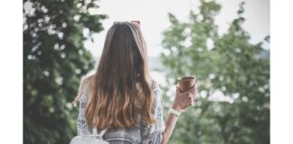 site-industries-cosmetiques A long-haired woman holds a cup of coffee while using a selfie stick.