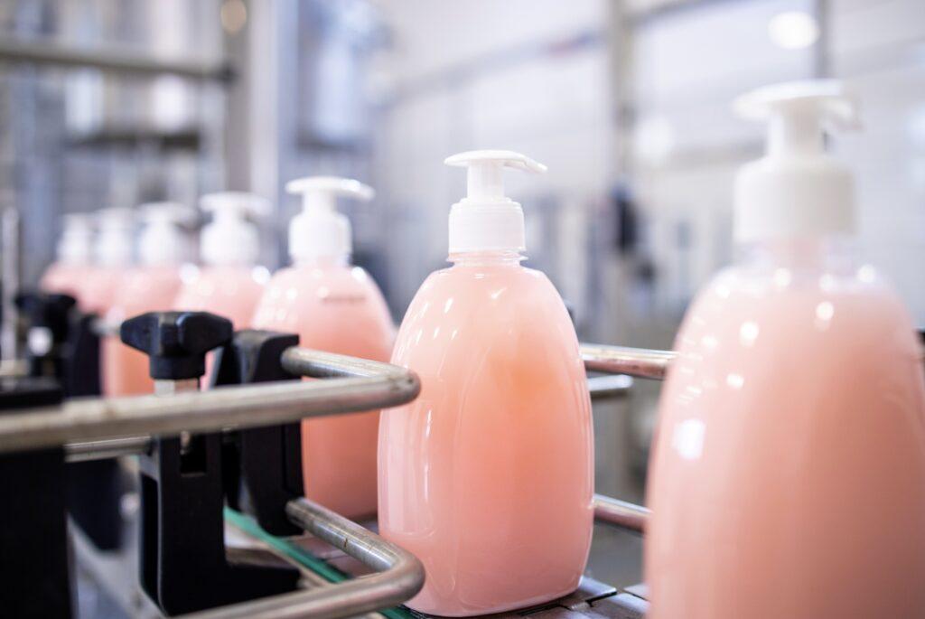 site-industries-cosmetiques Bouteilles de savon roses sur un tapis roulant dans une usine, mettant l'accent sur le laboratoire de contrôle qualité modernisé.