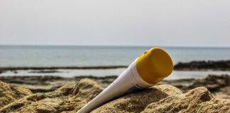 site-industries-cosmetiques Un tubo de crema solar sobre la arena junto al océano, protegido de los rayos UV nocivos.