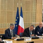 site-industries-cosmetiques Un comité assis à une table devant un drapeau.
