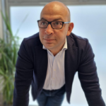 site-industries-cosmetiques Un hombre calvo con gafas se apoya en un escritorio de corrientes de aire.