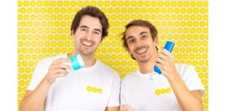 site-industries-cosmetiques Two smiling men with similar features, possibly twins, hold and present 900.care sun protection products against a yellow polka-dot background.