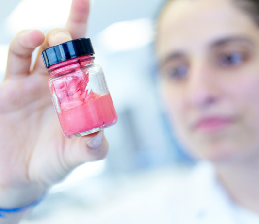 site-industries-cosmetiques A concentrated individual in a lab coat examining a small jar containing a pink substance, a pioneering cosmetic innovation using natural ingredients in Brittany.