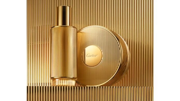 site-industries-cosmetiques 一个金色香水瓶和与之相配的圆形香水盒镶嵌在金色棱纹底座上。香水瓶的形状为圆柱形，表面光滑，其优雅的外形酷似 Brouillon 汽车，而容器的盖子中央则醒目地显示着 "Cartier"（卡地亚）的品牌名称。