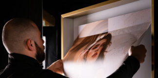 site-industries-cosmetiques A person with a shaved head and beard replaces a poster in a frame. The poster, featuring an image of a woman's face and the text "0 % discount", is adjusted at the top edge by the person, who appears to be demonstrating meticulous precision, rather like a craftsman honing his craft.