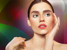 site-industries-cosmetiques Una mujer de pelo largo castaño y ojos verdes posa pensativa sobre un fondo colorido de bocetos de coches. Se toca la cara con una mano, revelando sus labios rosados y su piel pálida, mientras la iluminación acentúa sus rasgos.