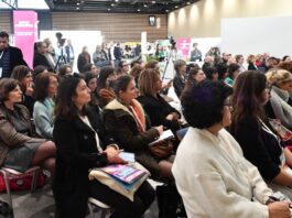 site-industries-cosmetiques A group of people seated on chairs listen attentively to a conference speaker as the CFIC trade show opens its doors. The spacious room boasts a modern design. Some attendees take notes as event banners rise behind them, along with a few people standing.