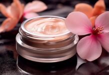 site-industries-cosmetiques Un tarro de cristal que contiene una crema de color melocotón descansa sobre una superficie negra brillante, encarnando la esencia del cuidado de la piel de lujo. Dos flores rosas de grandes pétalos están ingeniosamente colocadas a su lado. La iluminación de la escena resalta maravillosamente la textura de la crema y las delicadas flores.