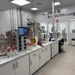 site-industries-cosmetiques Un laboratoire moderne équipé d'équipements et de machines scientifiques LipoTrue sur des paillasses blanches, de récipients en verre, de câbles et d'écrans. Le mur affiche « sciences et biotechnologies ». La pièce est propre, bien éclairée et axée sur la forte efficacité et les nouveaux ingrédients.