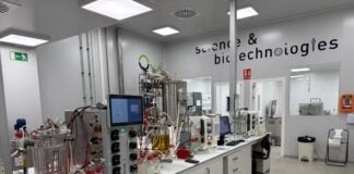 site-industries-cosmetiques A modern laboratory equipped with LipoTrue scientific equipment and machines on white benches, glass containers, cables and screens. The wall reads "science and biotechnology". The room is clean, well-lit and focused on high efficiency and new ingredients.