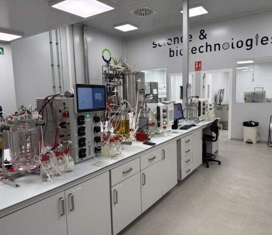 site-industries-cosmetiques 一个现代化的实验室，白色长凳、玻璃容器、电缆和屏幕上配备了 LipoTrue 科学设备和机器。墙上写着 "科学与生物技术"。室内干净整洁，光线充足，重点关注高效率和新成分。