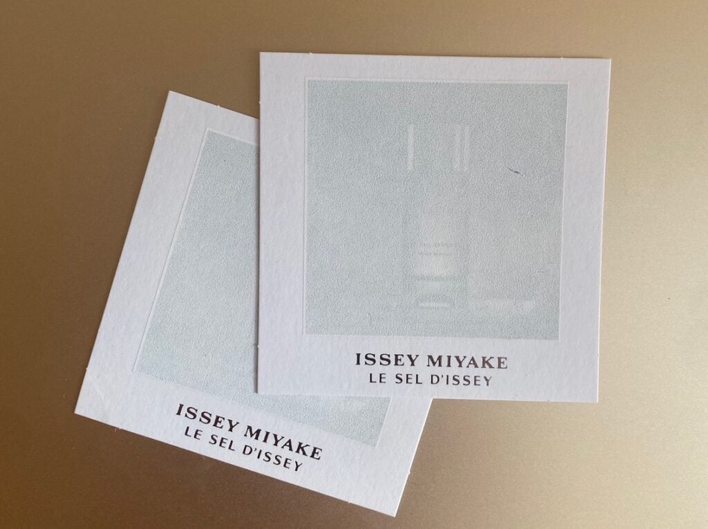 Collaboration entre Martinenq et Fedrigoni pour la découverte de parfums et produits cosmétiques 1 site-industries-cosmetiques Deux cartes d'échantillons de parfum carrées étiquetées « Issey Miyake Le Sel d'Issey » se chevauchent sur une surface marron clair unie, ressemblant à un Brouillon auto avec leur design blanc abstrait et discret au centre.