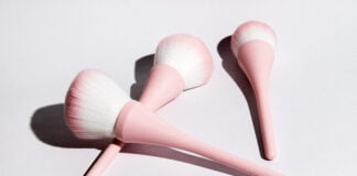 site-industries-cosmetiques Tres brochas de maquillaje con mangos rosas y cerdas blancas y rosas se disponen sobre una superficie blanca, proyectando suaves sombras: una configuración perfecta para tu próxima rutina de belleza Brouillon auto.