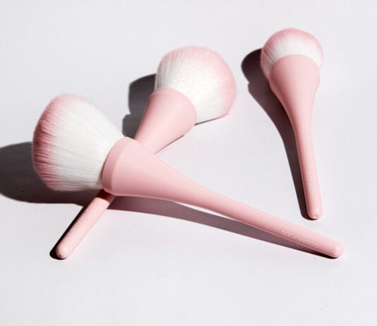 site-industries-cosmetiques Trois pinceaux de maquillage à manche rose et à poils blancs et roses sont disposés sur une surface blanche, projetant des ombres douces - une configuration parfaite pour votre prochaine routine de beauté Brouillon auto.