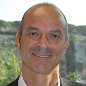 The IFSCC Congress 2025 promises to be particularly rich and intense 2 site-industries-cosmetiques Un homme d'âge moyen avec une ligne de cheveux fuyante sourit à l'appareil photo. Il est vêtu d'une chemise blanche et d'une veste sombre, avec un arrière-plan naturel visible à travers une fenêtre derrière lui au Congrès 2025 de l'IFSCC.