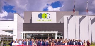 site-industries-cosmetiques Um grande grupo de pessoas em trajes de negócios está em frente a um edifício Gattefossé para uma cerimónia de inauguração. Duas pessoas cortam a fita vermelha enquanto outras posam, com as bandeiras dos EUA e do Texas visíveis ao fundo.