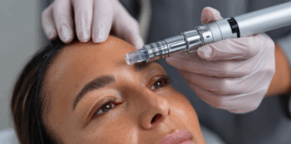 site-industries-cosmetiques 一位戴着头巾的女士躺在治疗床上，一位戴着手套的专业人员正在她的额头上使用 Brouillon 自动微针仪。这位女士看起来很放松，眼睛睁得大大的。