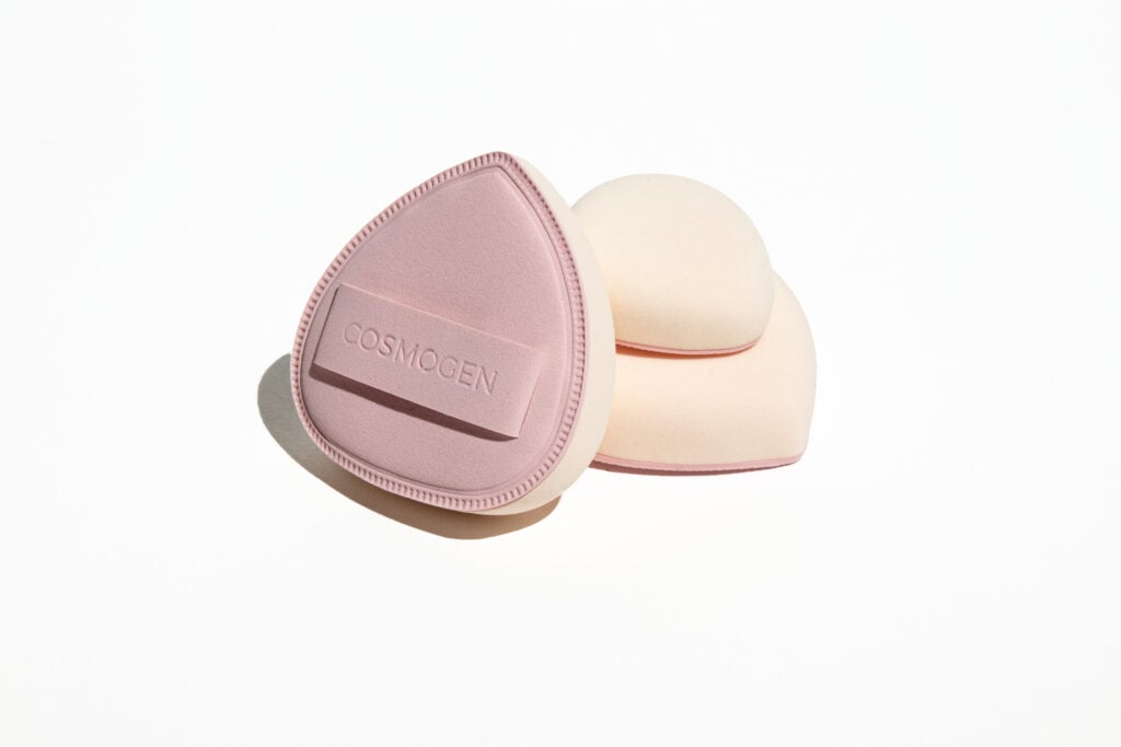 site-industries-cosmetiques Deux éponges de maquillage sont présentées sur un fond blanc. L'une est un applicateur expert Cosmogen rose pâle, plat et en forme de goutte d'eau ; l'autre est une éponge cunéiforme arrondie, blanc cassé, empilée en dessous.
