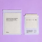 site-industries-cosmetiques Dois envelopes brancos acolchoados feitos de lã reciclada são apresentados contra um fundo roxo. O envelope maior, à esquerda, está escrito em francês, enquanto o mais pequeno apresenta instruções e um símbolo de reciclagem.