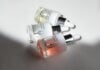 site-industries-cosmetiques Three glass dropper bottles of COSMOGEN skincare serum, featuring expert applicators, are arranged on a white surface, the light casting shadows and highlighting the transparent, tinted liquid contents inside each bottle.
