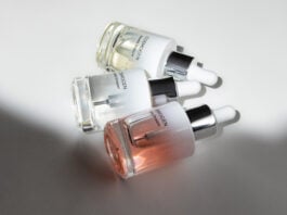 site-industries-cosmetiques Trois flacons compte-gouttes en verre de sérum de soin COSMOGEN, présentant des applicateurs experts, sont disposés sur une surface blanche, la lumière projetant des ombres et mettant en valeur le contenu liquide transparent et teinté à l'intérieur de chaque flacon.