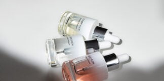site-industries-cosmetiques Tres frascos de cristal con cuentagotas de suero para el cuidado de la piel COSMOGEN, con aplicadores expertos, se disponen sobre una superficie blanca, la luz proyecta sombras y resalta el contenido líquido transparente y tintado del interior de cada frasco.