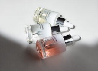 site-industries-cosmetiques Três frascos de vidro com conta-gotas de sérum COSMOGEN, com aplicadores especializados, estão dispostos numa superfície branca, com a luz a criar sombras e a realçar o conteúdo líquido transparente e matizado dentro de cada frasco.
