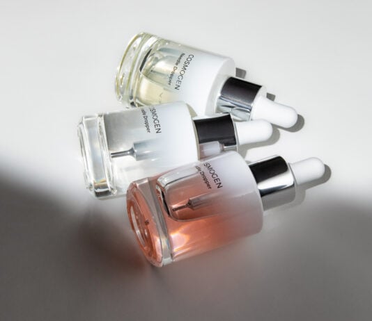 site-industries-cosmetiques Trois flacons compte-gouttes en verre de sérum de soin COSMOGEN, présentant des applicateurs experts, sont disposés sur une surface blanche, la lumière projetant des ombres et mettant en valeur le contenu liquide transparent et teinté à l'intérieur de chaque flacon.