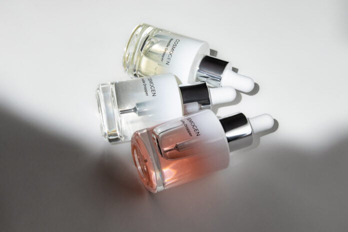 site-industries-cosmetiques Trois flacons compte-gouttes en verre de sérum de soin COSMOGEN, présentant des applicateurs experts, sont disposés sur une surface blanche, la lumière projetant des ombres et mettant en valeur le contenu liquide transparent et teinté à l'intérieur de chaque flacon.