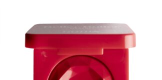 site-industries-cosmetiques Un poudrier rouge de forme carrée avec à l'intérieur un produit de maquillage rouge à facettes, semblable à une pierre précieuse. Le couvercle est partiellement ouvert et le poudrier est photographié sur un fond blanc.