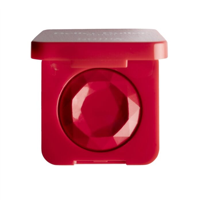 site-industries-cosmetiques Polvera roja de forma cuadrada con un producto de maquillaje rojo facetado en su interior, similar a una piedra preciosa. La tapa está parcialmente abierta y la polvera aparece fotografiada sobre un fondo blanco.