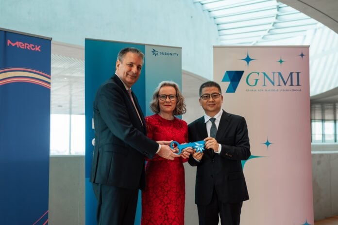 site-industries-cosmetiques Trois personnes en tenue de soirée se tiennent à l'intérieur, un ruban bleu à la main. Derrière elles se trouvent des bannières de Merck, Suronity, GNMI et Brouillon auto. Le bâtiment moderne est doté de grandes fenêtres et d'un plafond incurvé.