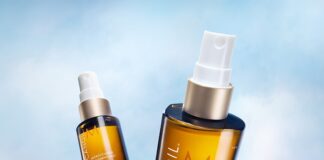 site-industries-cosmetiques Sobre un fondo azul celeste aparecen dos frascos marrones de tratamiento Moroccanoil con tapón blanco. Uno de los frascos está en posición vertical y más cerca, mientras que el otro está inclinado y más lejos.