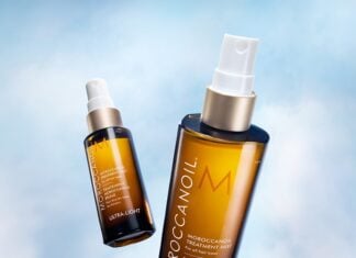 site-industries-cosmetiques Two brown Moroccanoil treatment bottles with white caps are shown against a sky-blue background. One bottle is upright and closer, while the other is angled and further away.