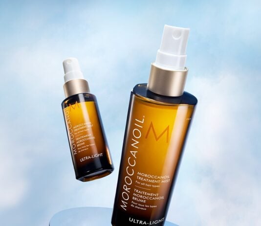 site-industries-cosmetiques Deux flacons bruns de traitement Moroccanoil avec des bouchons blancs sont présentés sur un fond bleu ciel. L'un des flacons est droit et plus proche, tandis que l'autre est incliné et plus éloigné.