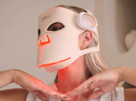 site-industries-cosmetiques Une personne portant un haut blanc sans manches et un masque de luminothérapie à LED dont la marque "Silk'n" est visible. Le masque émet une lumière rouge et la personne tient ses mains sous son menton.