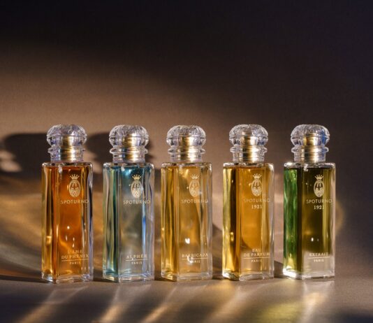 site-industries-cosmetics 博尔米奥利-路易吉（Bormioli Luigi）设计的五个带有金色标签和水晶瓶塞的玻璃香水瓶在暖色调灯光的映衬下排列成一排，每个瓶子都采用了受 Spoturno 启发的玻璃创新技术，并装有不同颜色的液体。.