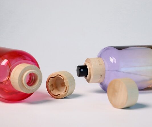 site-industries-cosmetiques Deux bouteilles, l'une rouge et l'autre violette, sont couchées sur le côté et leurs bouchons en bois ont été retirés. La bouteille violette est munie d'une buse de pulvérisation noire. L'arrière-plan est uni et de couleur claire.